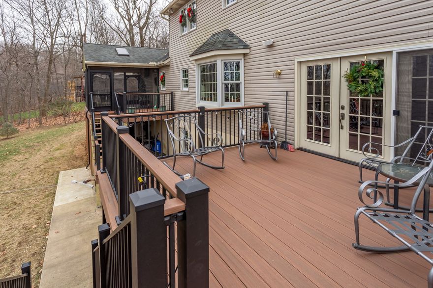 Deck with black railing beside beige house, rocking chair, and glass doors overlooking wooded yard