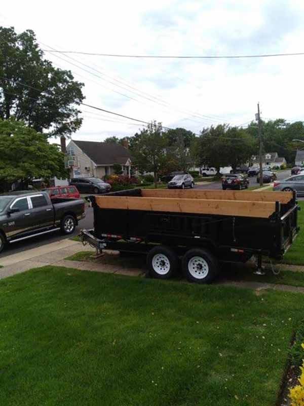 A dumpster trailer is parked in a driveway next to a truck.