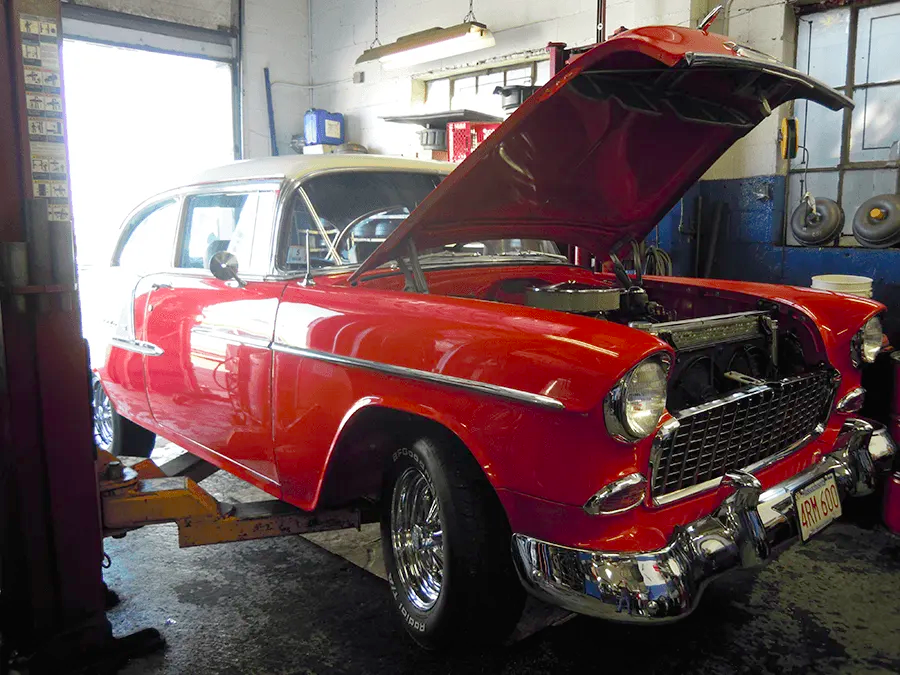 A red car with the hood up in a garage