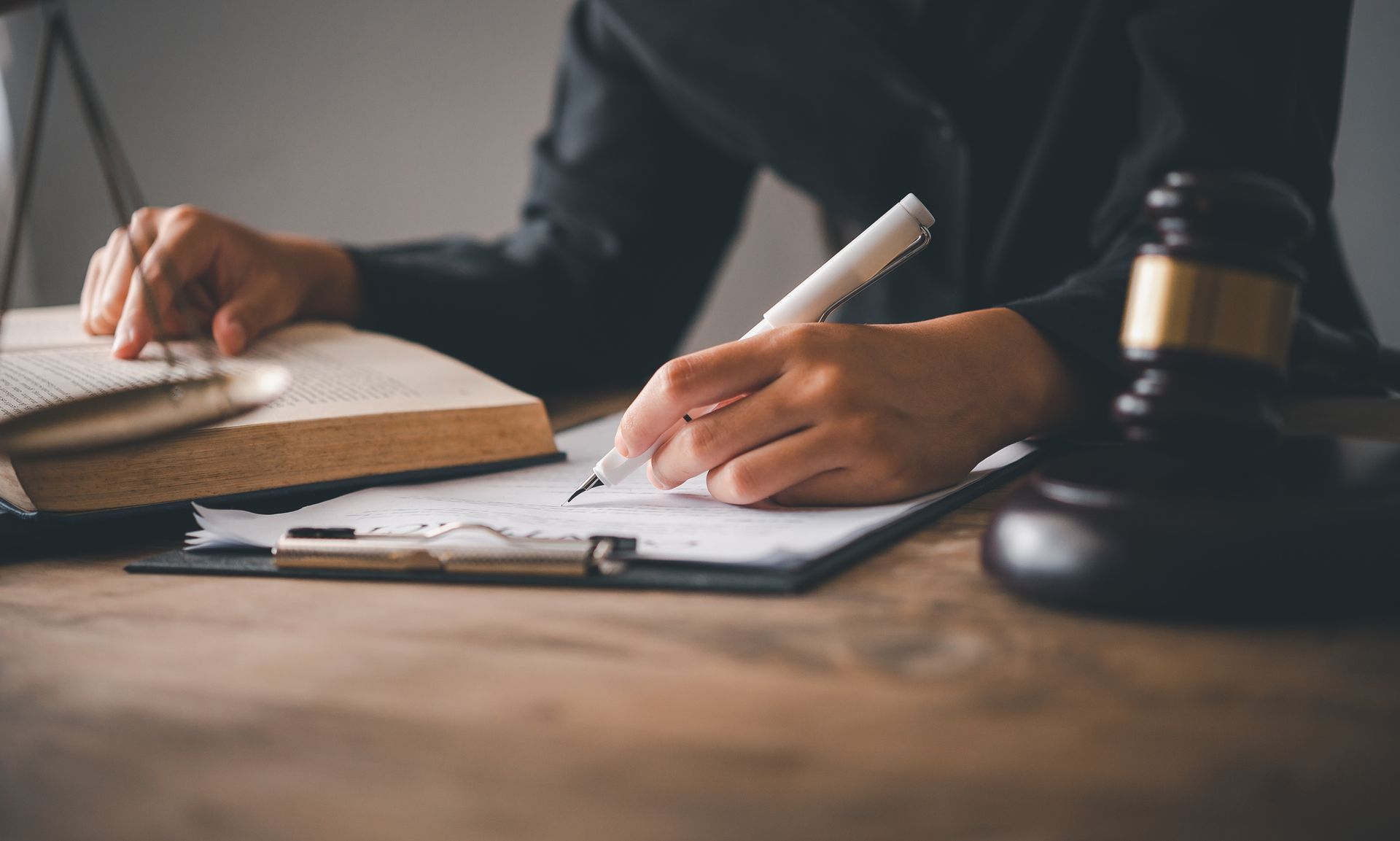 Lawyer writing legal notes with open book and judge gavel on wooden desk. Lawyer writing legal notes with open book and judge gavel on wooden desk.