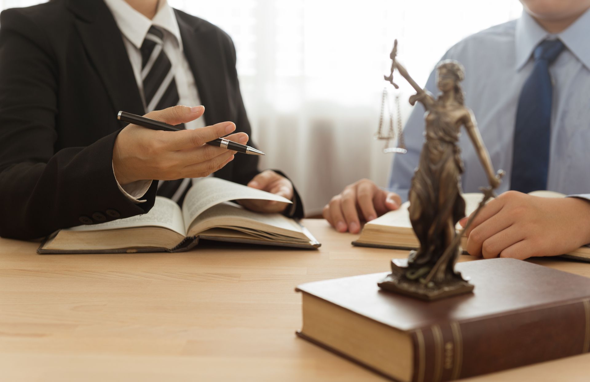 Lawyers discussing legal case with books and Lady Justice statue on office desk. Lawyers discussing legal case with books and Lady Justice statue on office desk.