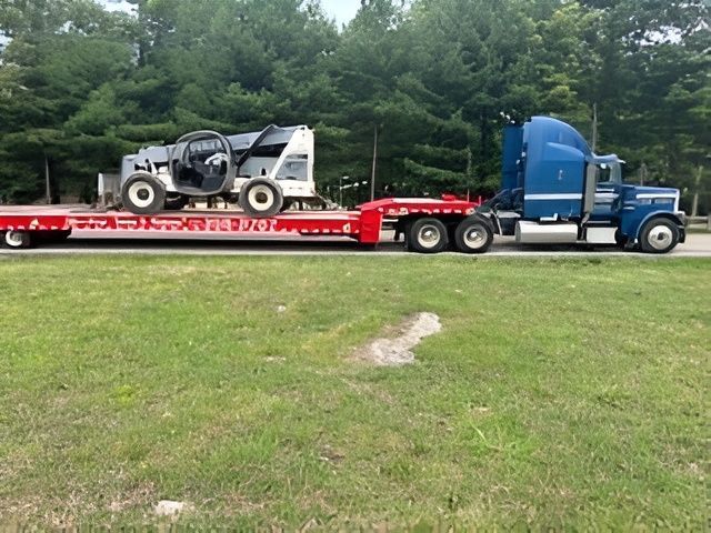 Semi-truck transporting heavy machinery on a flatbed trailer, roadside.