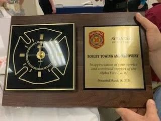 Fire department plaque for Bosley Towing, with a clock and an inscription, held by a person.