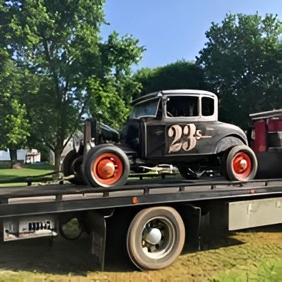 Vintage black race car, number 23, on a tow truck, red wheels, outdoors.