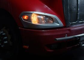 Red semi-truck's headlight illuminated, with turn signal flashing.