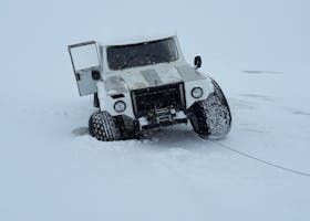White vehicle stuck in deep snow, door open. A tow cable is visible.