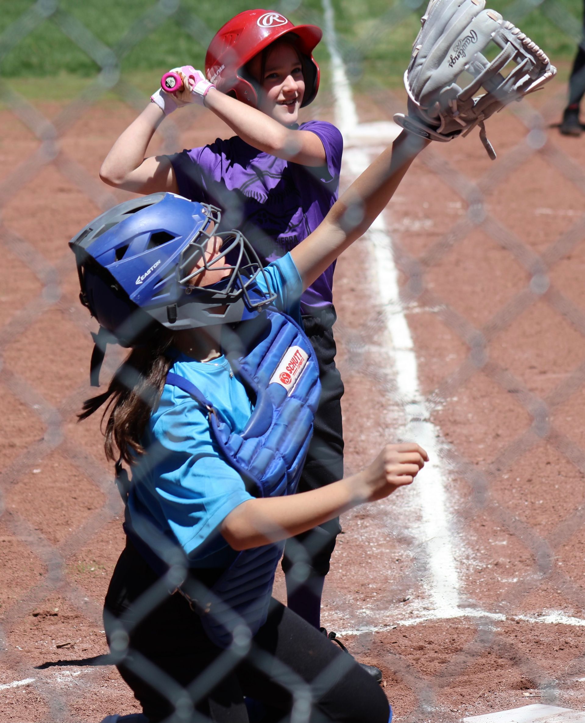 A person wearing a hat and orange shirt, holding a baseball bat on their shoulder on a baseball field.