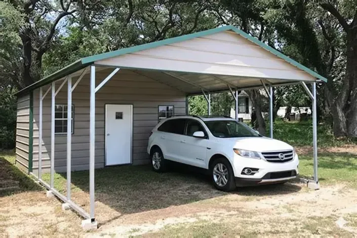 White car parked under a metal carport beside a small shed in a wooded yard
