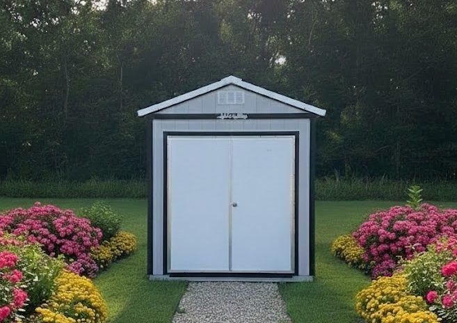 Small white shed with double doors in a landscaped garden, bordered by pink and yellow flowers.