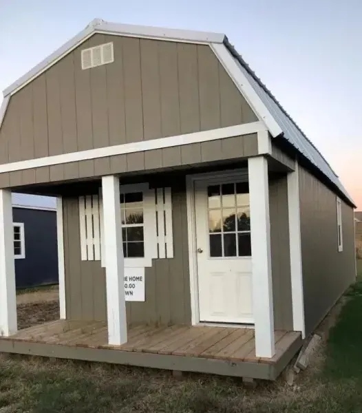Small beige shed-style house with white trim and a front porch on a grassy lot