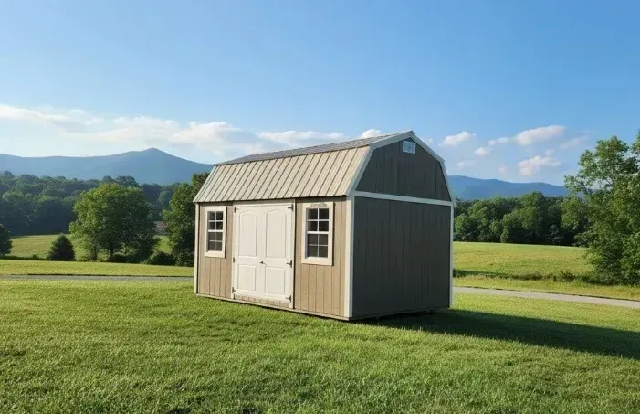 Small beige shed with white double doors on a grassy field, mountains and blue sky in the background