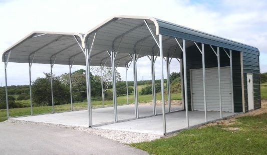 Covered metal parking shelter with two bays on a gravel pad beside a grassy roadside.