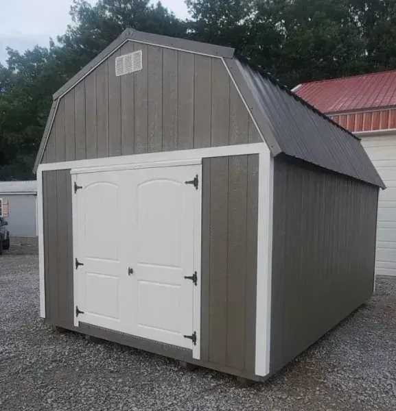 Gray barn-style storage shed with white double doors and a red roof, sitting on gravel outdoors