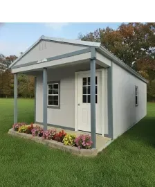 Small white house with gray trim and porch, surrounded by grass and flowers