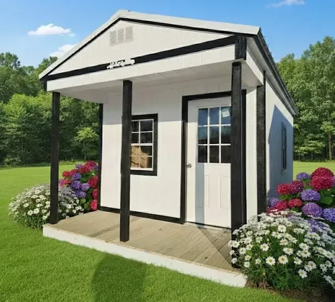 Small white shed with black trim and flowers in a grassy yard