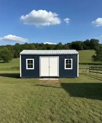 Small navy shed with white double doors and windows in a grassy field under a blue sky with clouds
