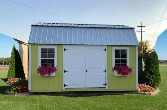 Small yellow garden shed with white double doors, window box flowers, and flower beds in a grassy yard.