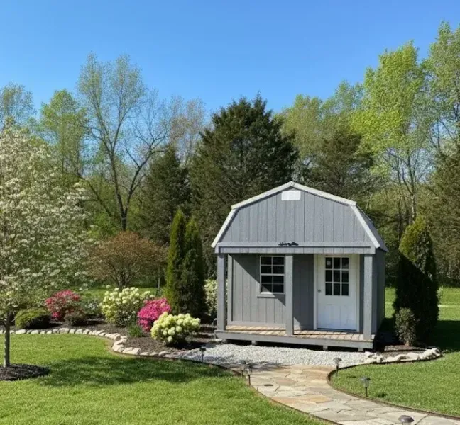 Small gray garden shed with white trim in a landscaped backyard under a blue sky