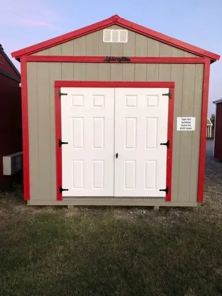 Small gray shed with red trim and white double doors on grass.
