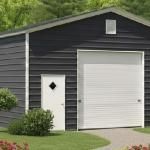 Dark gray garage with white door and small side entry door, surrounded by green lawn and shrubs
