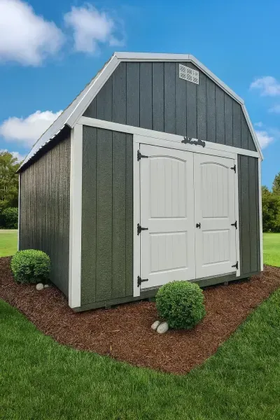 Gray garden shed with white double doors and green trim on a grassy lawn under a blue sky