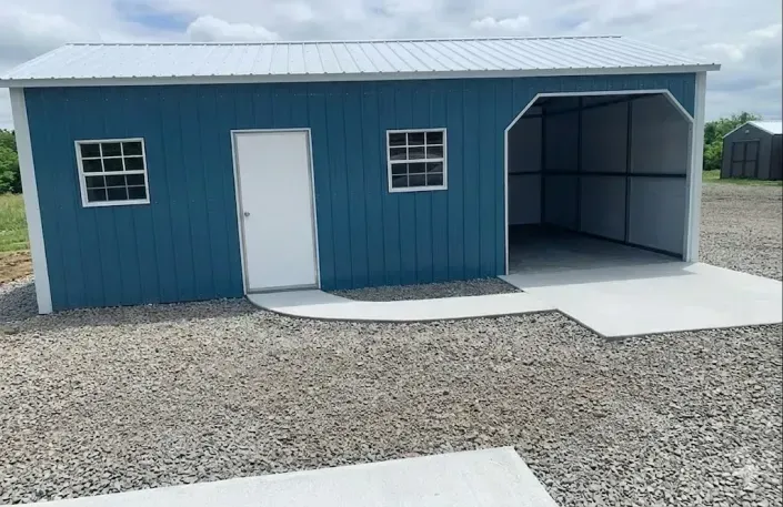 Blue metal shed with white doors and gravel driveway, open garage bay on the right.