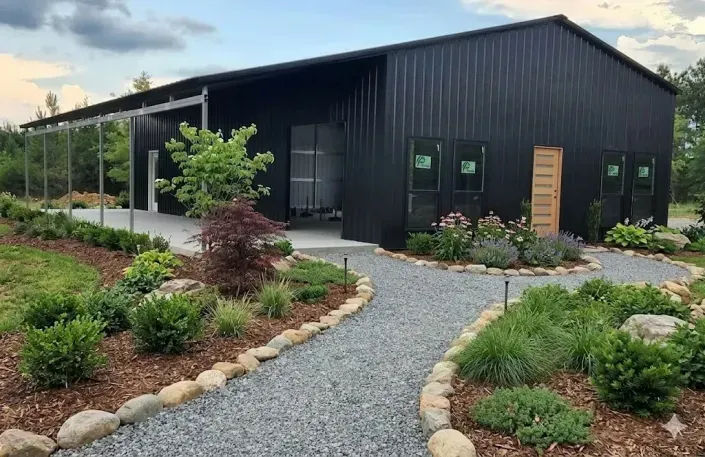Modern black barn-style building with gravel path and landscaped garden beds
