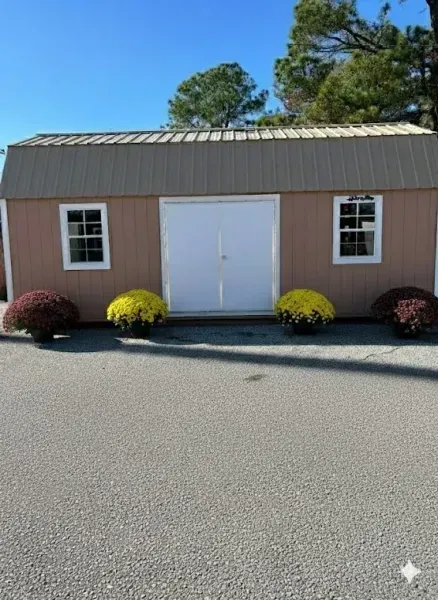 Small brown shed with white double doors and windows, fronted by yellow and red shrubs on a sunny day