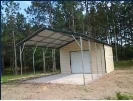 Small beige metal shed with attached open carport on a dirt lot, backed by pine trees.