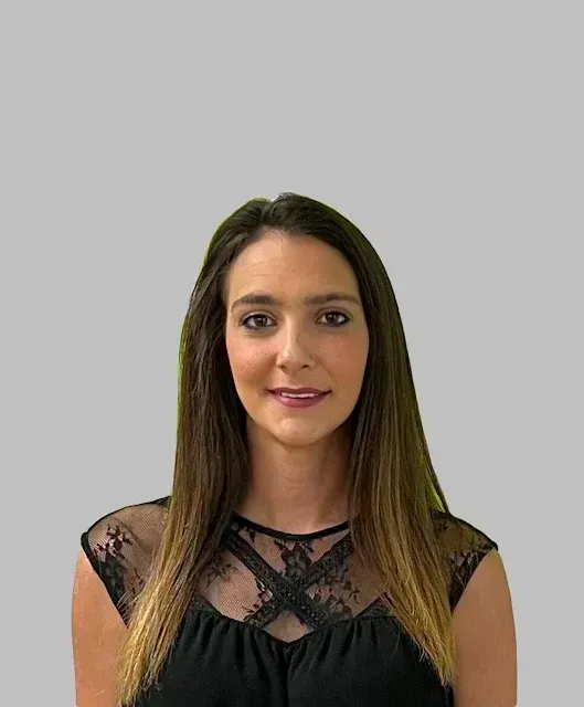 Woman with long brown hair, wearing a black lace top, smiling at the camera.