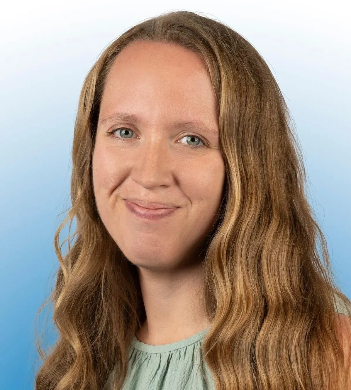 Woman with long wavy brown hair, smiling, light blue eyes, light green top.