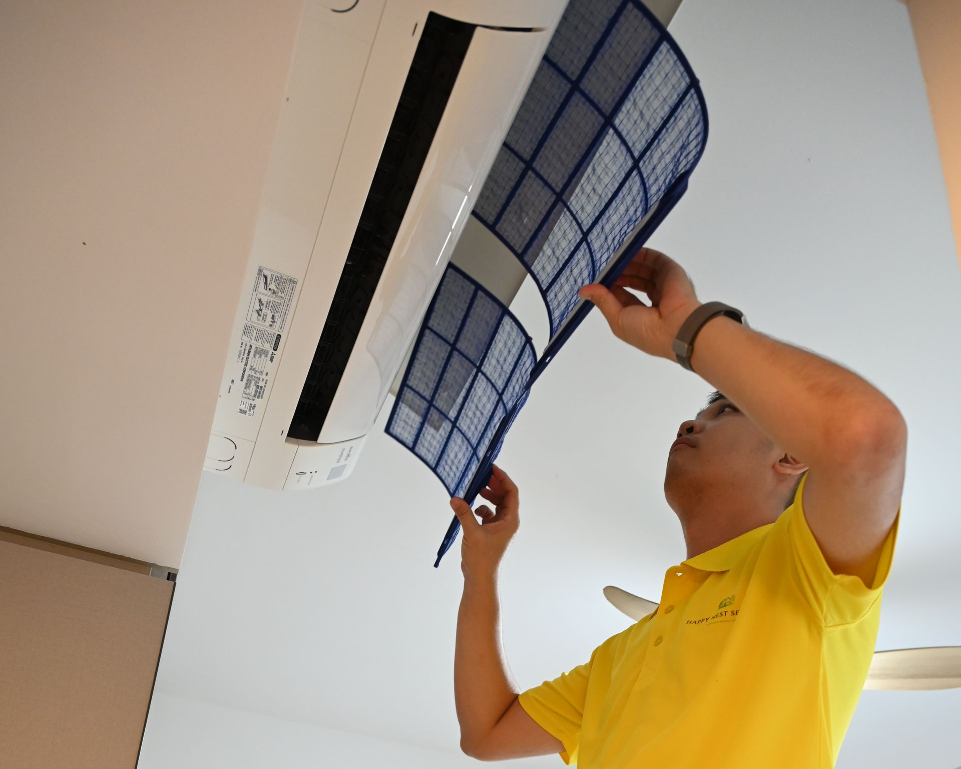 Man in yellow shirt removes air filter from  air conditioner.
