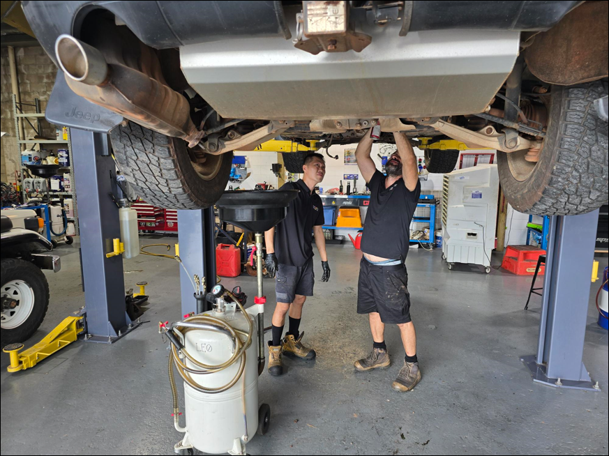 Two mechanics work beneath a raised car in a garage - Darwin Auto Mobile Care in Woolner, NT