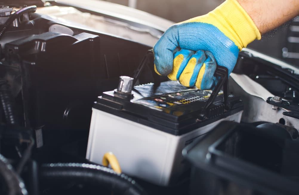 A Person Lifts A Car Battery From A Vehicle's Engine Bay — Darwin Auto Mobile Care in Woolner, NT