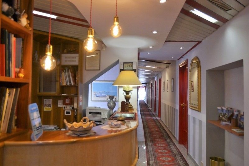 Reception dell'hotel con illuminazione dall'alto, corridoio con porte rosse e un lungo tappeto.