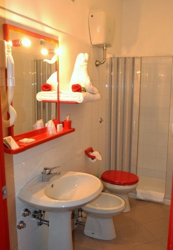 Bagno rosso e bianco brillante con lavandino, WC, doccia e sistema di asciugamani.