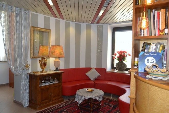 Accogliente hall dell'hotel con divano rosso curvo, parete a strisce, mobile antico e un tavolino rotondo.