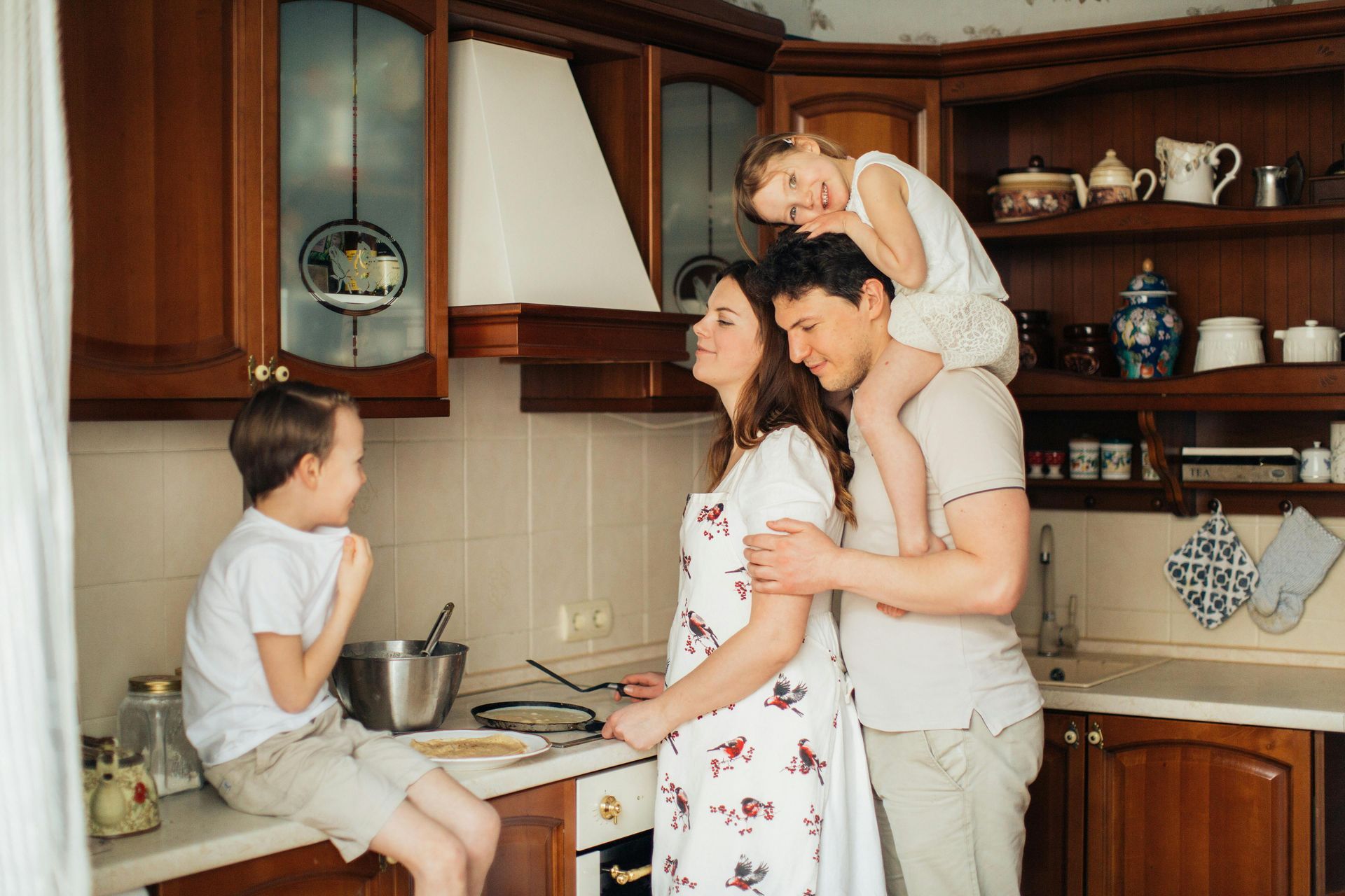 A family is standing in a kitchen with two children and a pregnant woman.