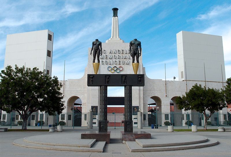 Memorial Coliseum entrance with Olympic statues and torch, flanked by white towers, Los Angeles.