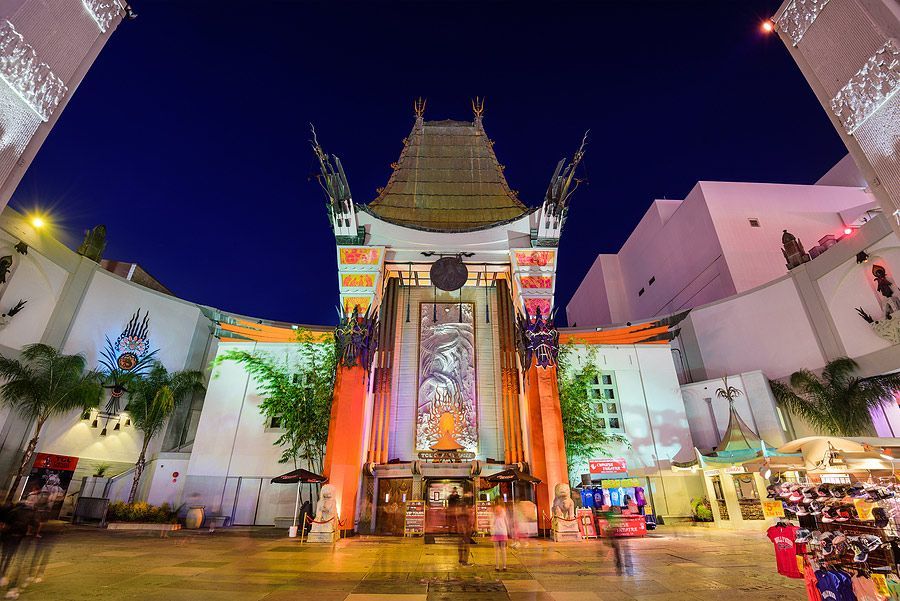 TCL Chinese Theatre entrance at night. Red, white, and gold colors. People walking in the plaza.