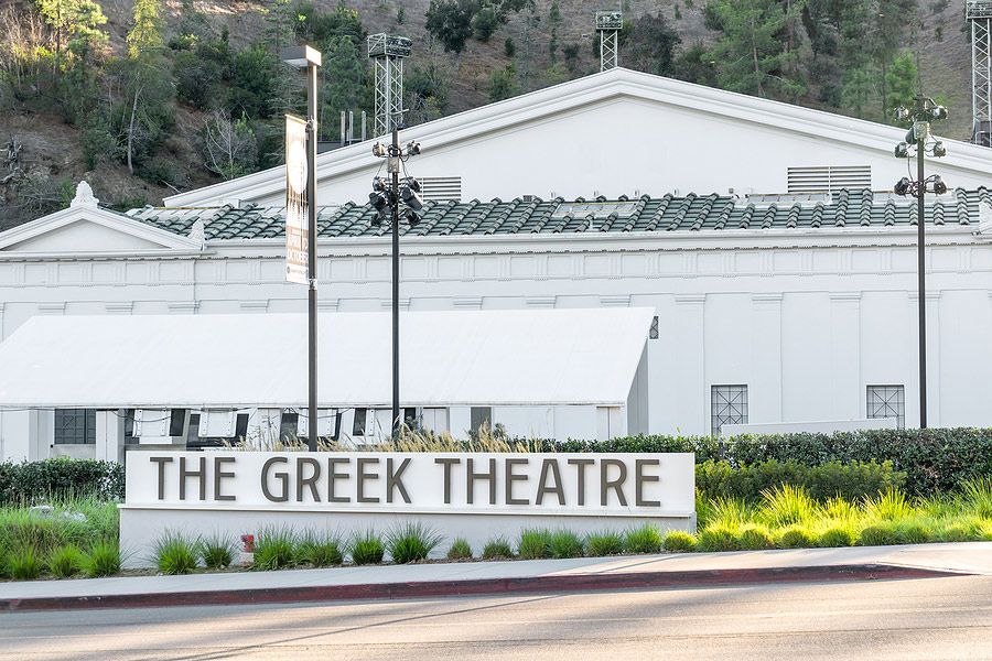 The Greek Theatre sign in front of a white building with a green roof, mountains in the background.