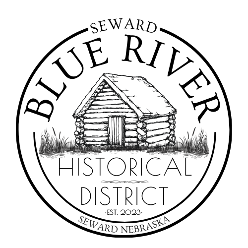 Circular logo for Blue River Historical District in Seward, Nebraska, featuring a log cabin and text.