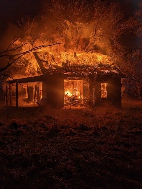 House engulfed in flames at night, orange fire illuminating the dark landscape.