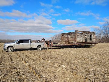 Pickup truck towing a flatbed trailer with stacked wooden crates across a harvested field under a blue sky