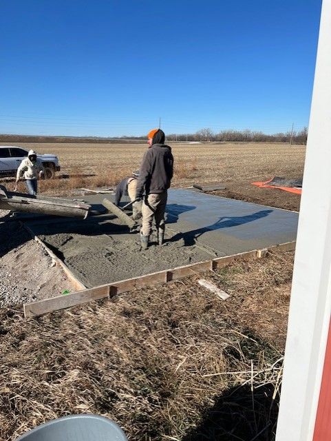 Construction workers pouring concrete for a slab on a field on a sunny day.