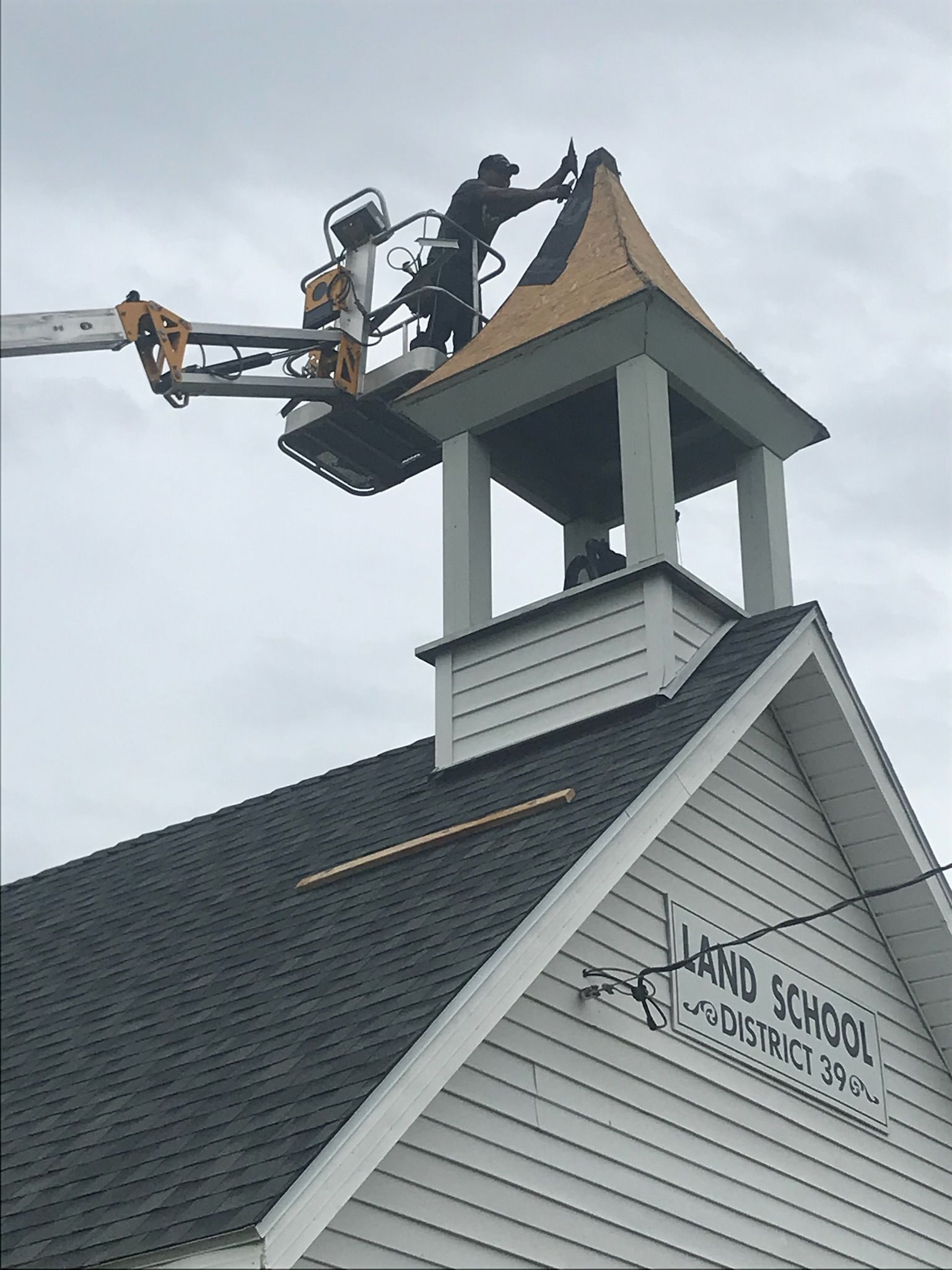 Workers in a lift repair the bell tower roof of the
