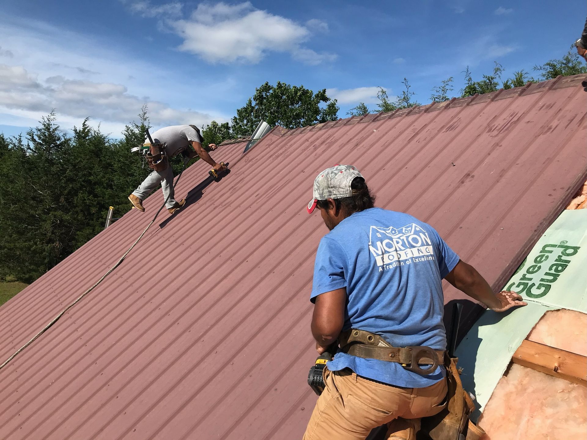 Two roofers installing a red metal roof on a sunny day.