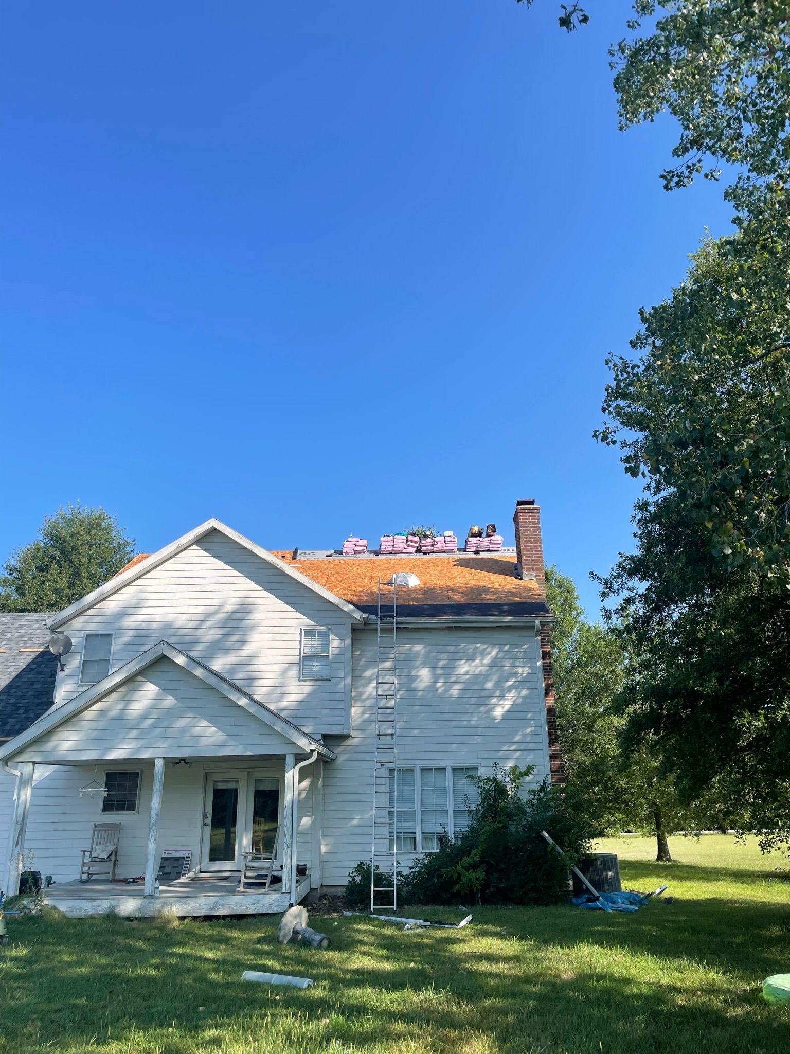 White house with partially removed roof; blue sky; green grass and trees.