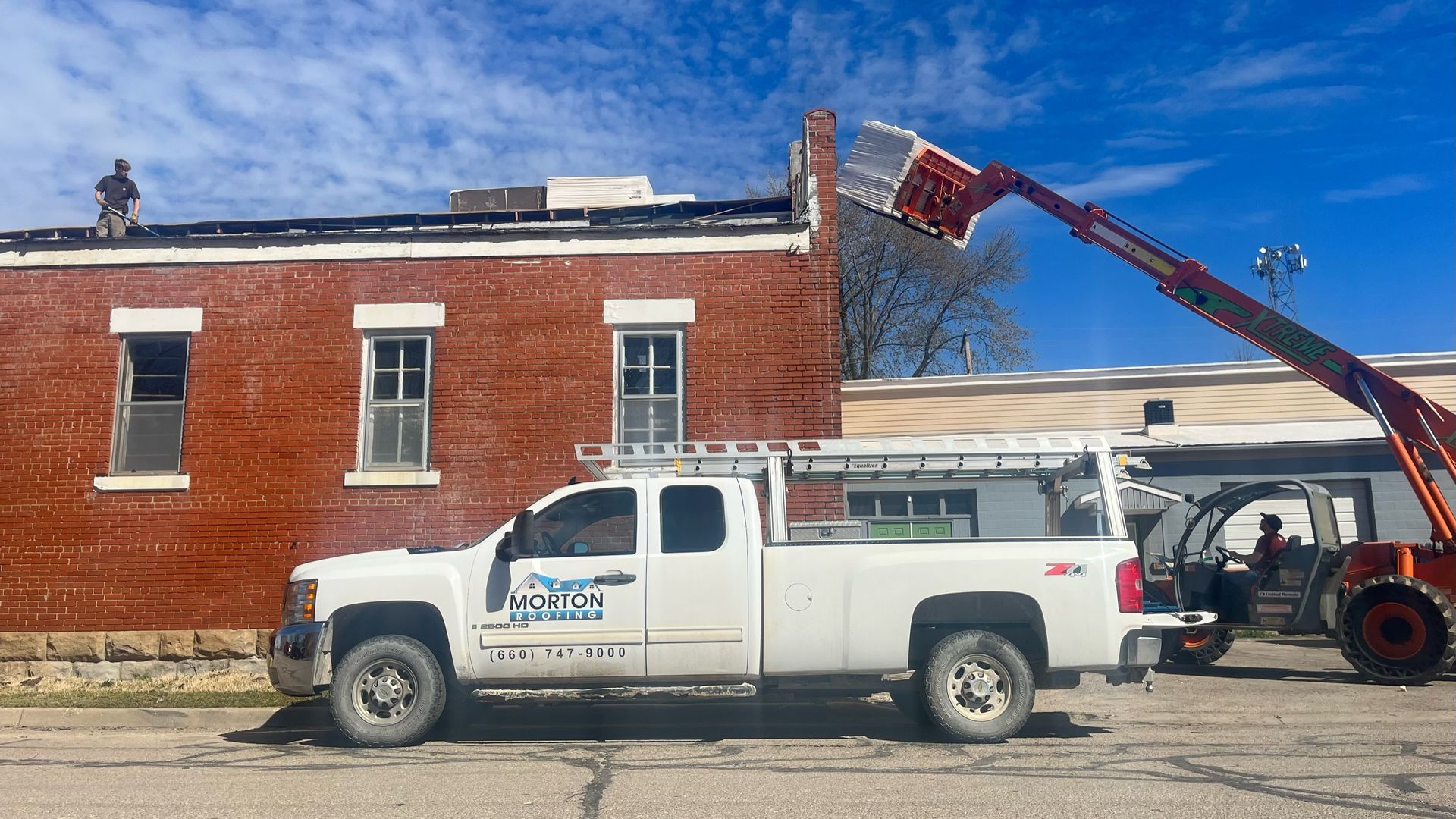 White truck parked near brick building as workers repair roof with lift.