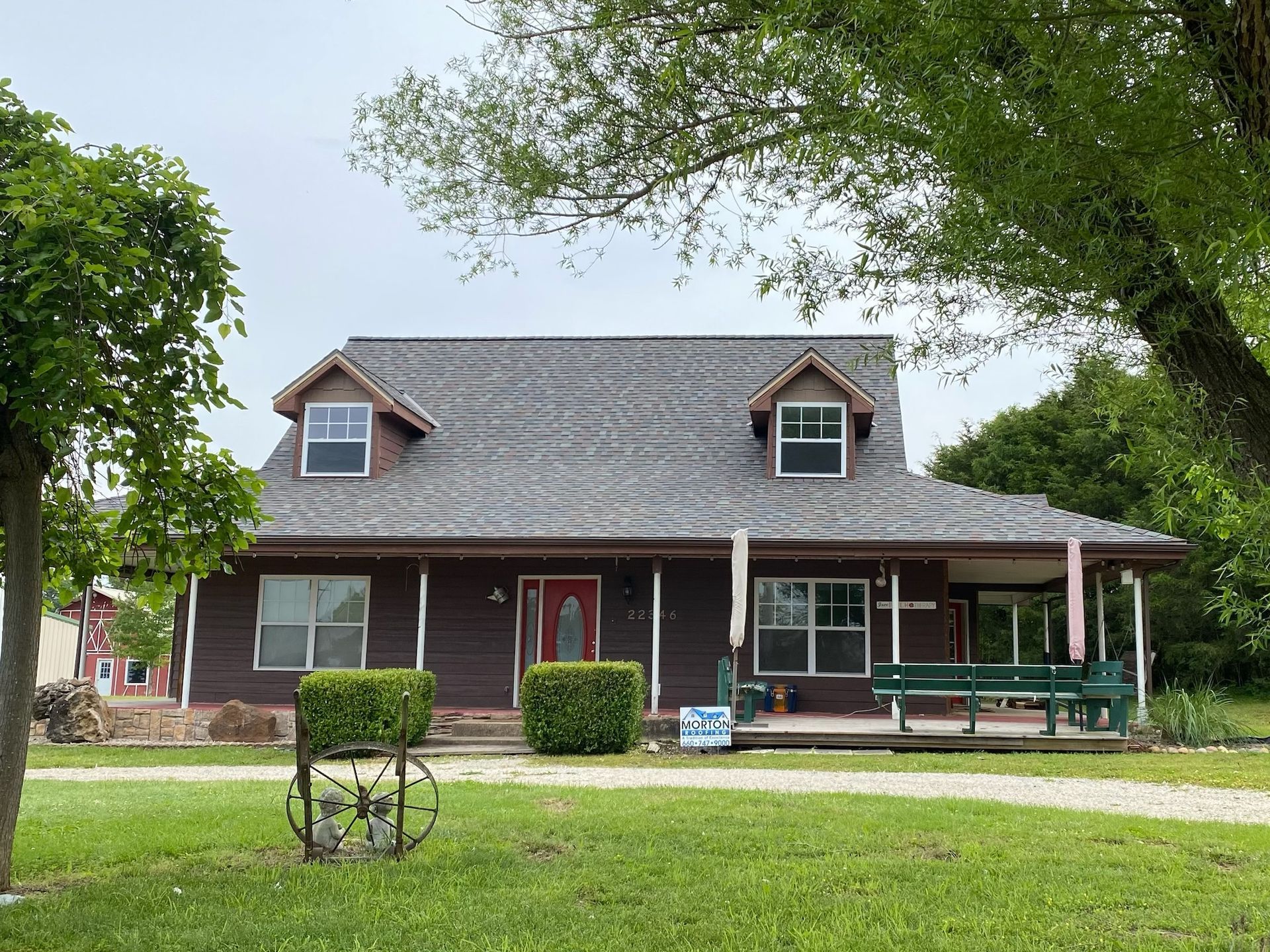Brown house with porch, two dormers, and green lawn, trees.